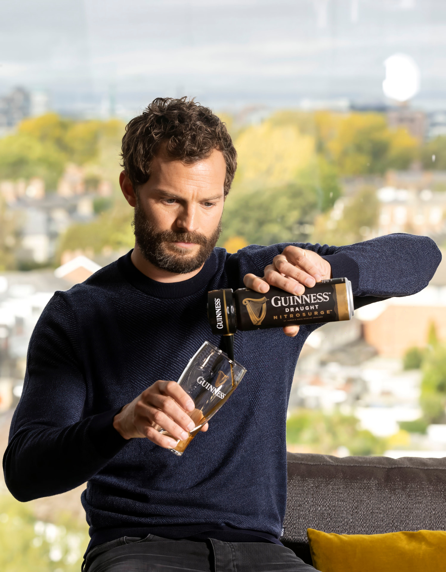 Jamie Dornan pouring Guinness from a bottle into a pint glass outdoors