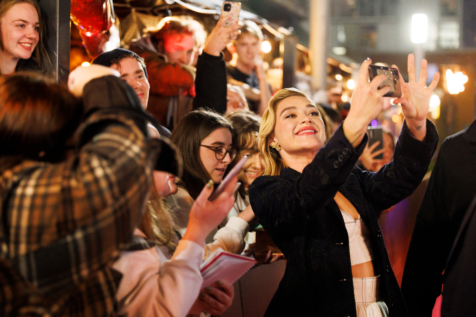 Florence Pugh leaning towards a crowd of fans to take a selfie as they hold up their phones